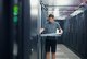 Ein Mann steht in einem Serverraum zwischen Serverschränken und arbeitet an einer Schublade mit Hardware.