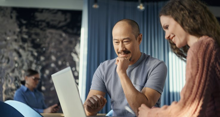 Ein Mann und eine Frau sitzen nebeneinander an einem Tisch und schauen gemeinsam auf einen aufgeklappten Laptop.